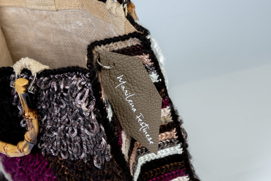 Morbida e dai colori che richiamano l'autunno, filo dopo filo, si compone in nove quadratoni una Tote bag unica nel suo genere. I manici in bambù, uno dei simboli identificativi del brand, permettono di indossarla come borsa a mano; La sua tracolla rimovibile, invece, permette di portare la borsa a spalla. Di manifattura artigianale, prodotta in Italia.