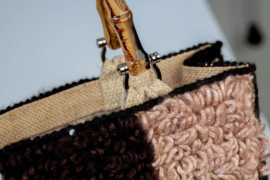 Morbida e dai colori che richiamano l'autunno, filo dopo filo, si compone in nove quadratoni una Tote bag unica nel suo genere. I manici in bambù, uno dei simboli identificativi del brand, permettono di indossarla come borsa a mano; La sua tracolla rimovibile, invece, permette di portare la borsa a spalla. Di manifattura artigianale, prodotta in Italia.