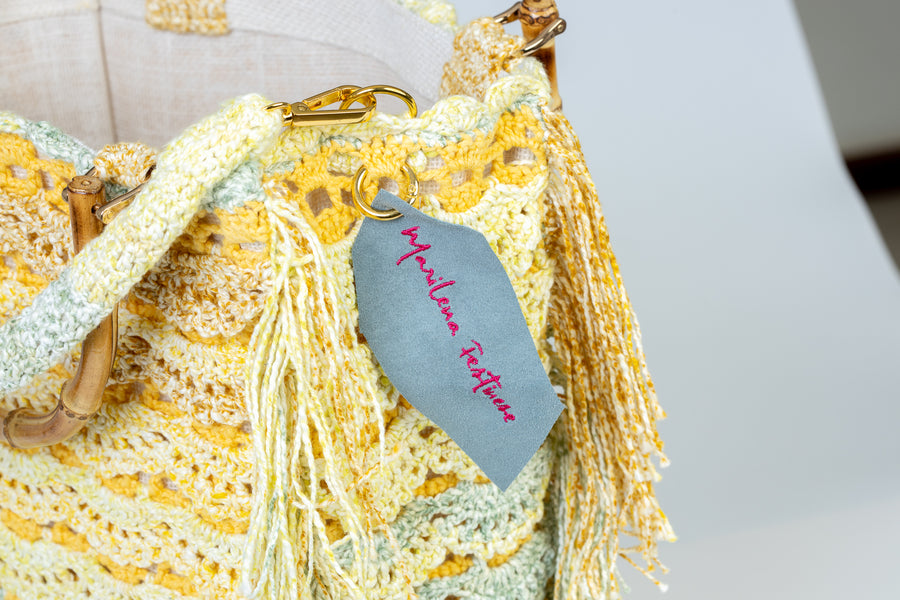 Realizzata ad uncinetto, questa tote bag si presenta con una base a rete e dei punti a ventaglio in rilievo. I manici in bambù, uno dei simboli identificativi del brand, permettono di indossarla come borsa a mano; Un manico più lungo, realizzato mediante uncinetto, permette di portarla a spalla. Di manifattura artigianale, prodotta in Italia.