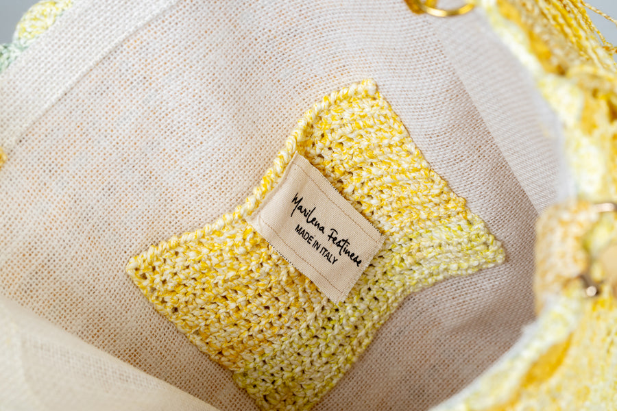 Realizzata ad uncinetto, questa tote bag si presenta con una base a rete e dei punti a ventaglio in rilievo. I manici in bambù, uno dei simboli identificativi del brand, permettono di indossarla come borsa a mano; Un manico più lungo, realizzato mediante uncinetto, permette di portarla a spalla. Di manifattura artigianale, prodotta in Italia.