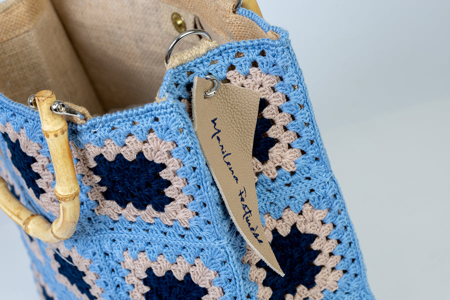 Questa Tote bag dal design patchwork è realizzata ad uncinetto. Elementi di spicco composti da mattonelle ispirate alle maioliche dei palazzi del centro. I manici in bambù, uno dei simboli identificativi del brand, permettono di indossarla come borsa a mano; La sua tracolla rimovibile, invece, permette di portare la borsa a spalla. Di manifattura artigianale, prodotta in Italia