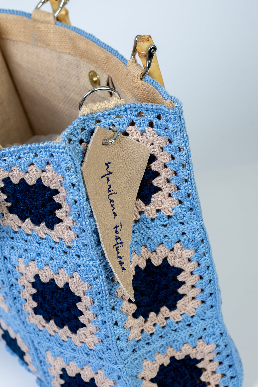 Questa Tote bag dal design patchwork è realizzata ad uncinetto. Elementi di spicco composti da mattonelle ispirate alle maioliche dei palazzi del centro. I manici in bambù, uno dei simboli identificativi del brand, permettono di indossarla come borsa a mano; La sua tracolla rimovibile, invece, permette di portare la borsa a spalla. Di manifattura artigianale, prodotta in Italia
