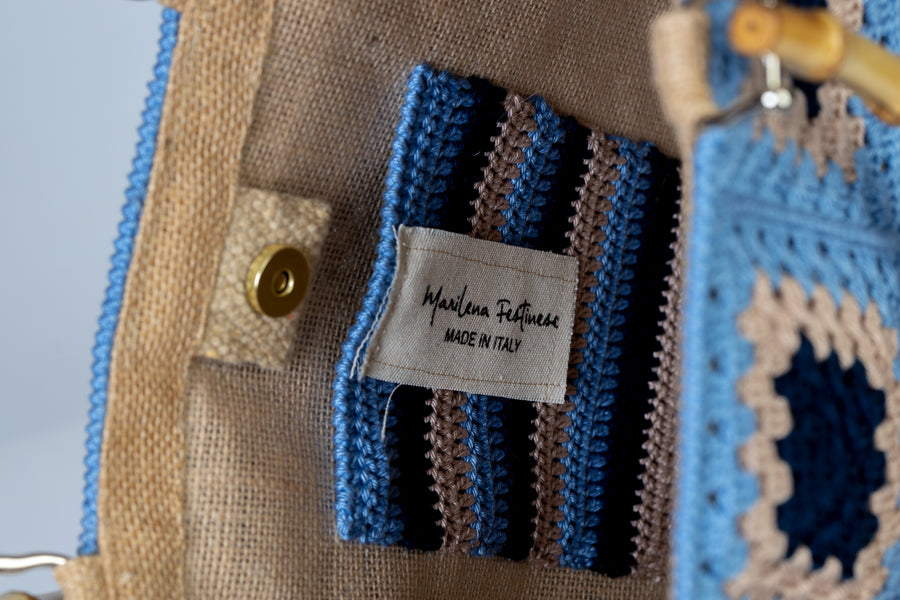 Questa Tote bag dal design patchwork è realizzata ad uncinetto. Elementi di spicco composti da mattonelle ispirate alle maioliche dei palazzi del centro. I manici in bambù, uno dei simboli identificativi del brand, permettono di indossarla come borsa a mano; La sua tracolla rimovibile, invece, permette di portare la borsa a spalla. Di manifattura artigianale, prodotta in Italia